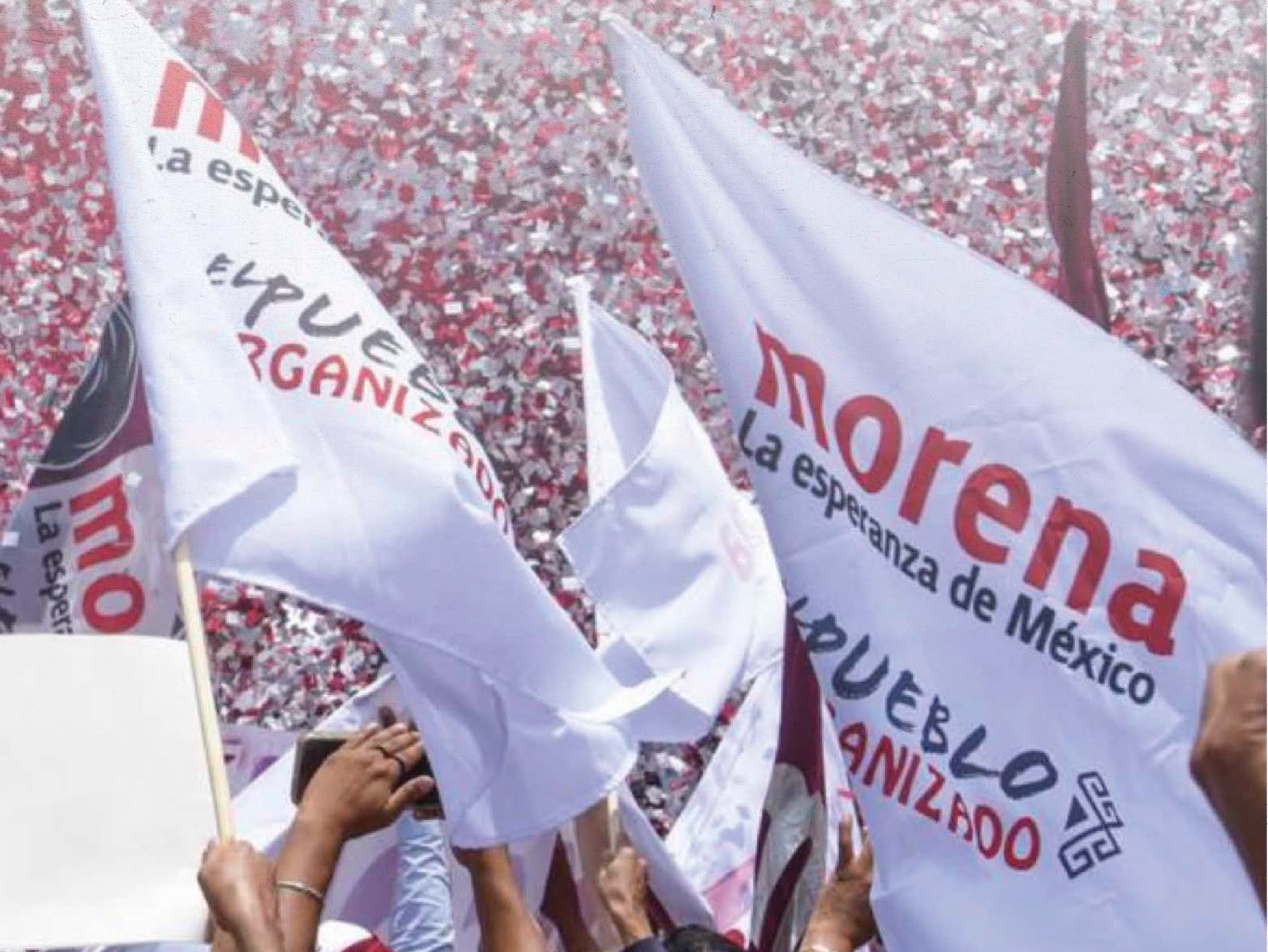 Banderas blancas con el nombre y emblema de Morena ondean frente a una multitud durante un acto político