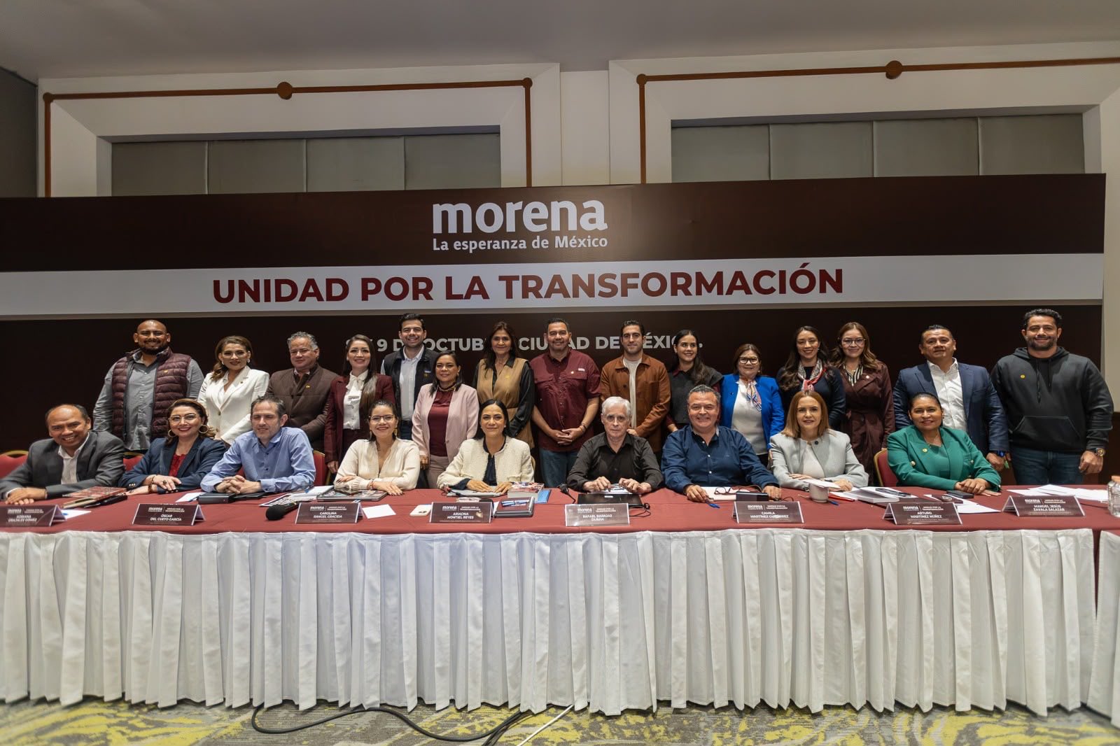 Grupo de participantes posa detrás de una mesa ante un panel con los emblemas de Morena y el lema Unidad por la Transformación.