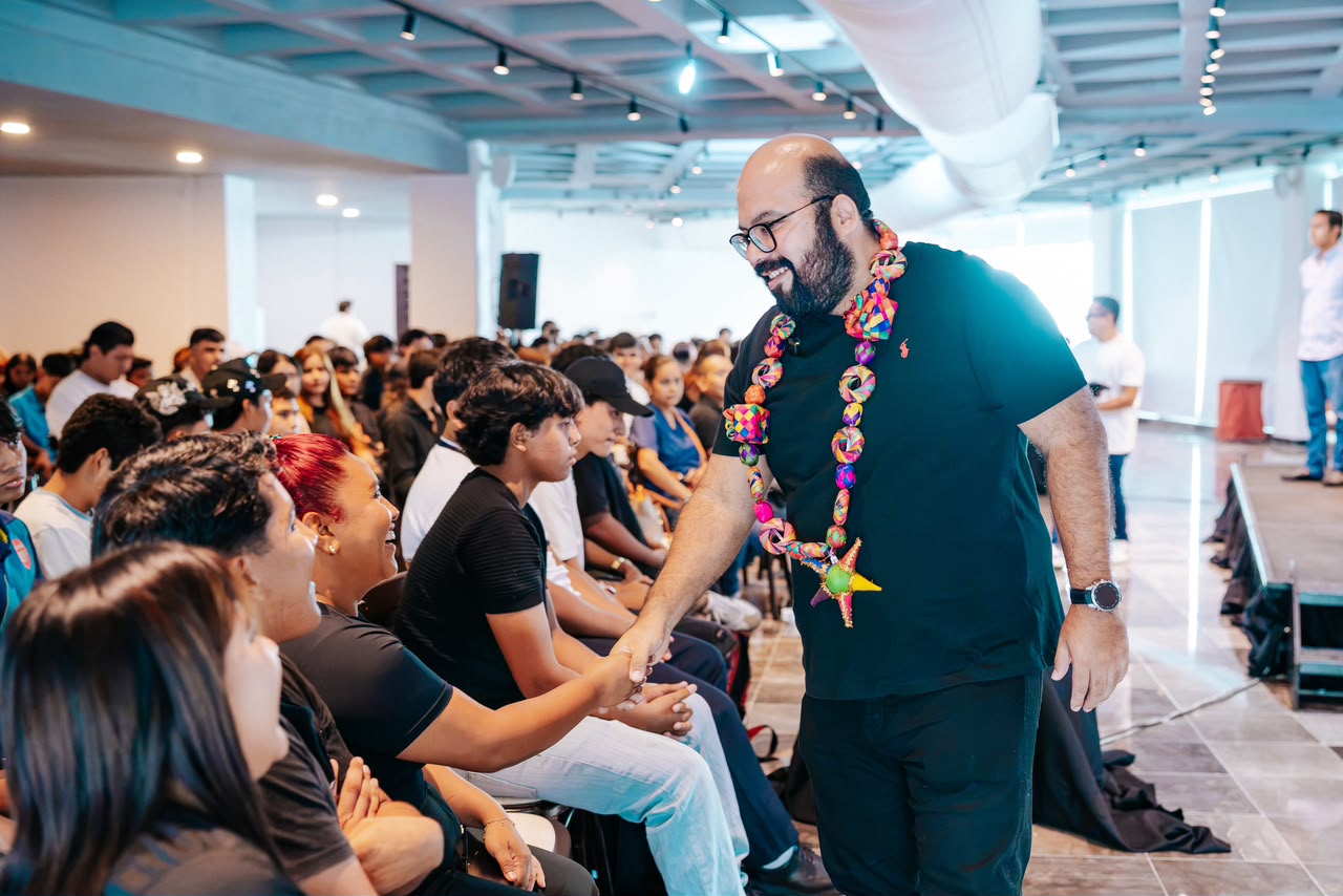 Grupo numeroso de jóvenes y adultos reunidos en un salón para una fotografía colectiva con Ricardo Salinas Méndez