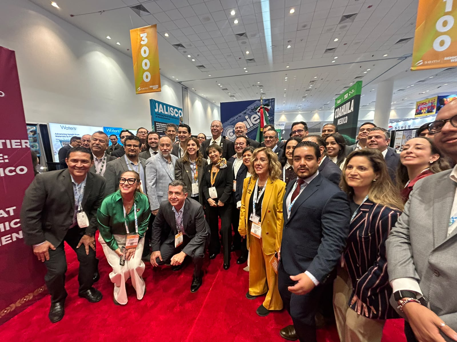Grupo de representantes y asistentes posan en una feria tecnológica ante letreros de Jalisco y Coahuila, México.