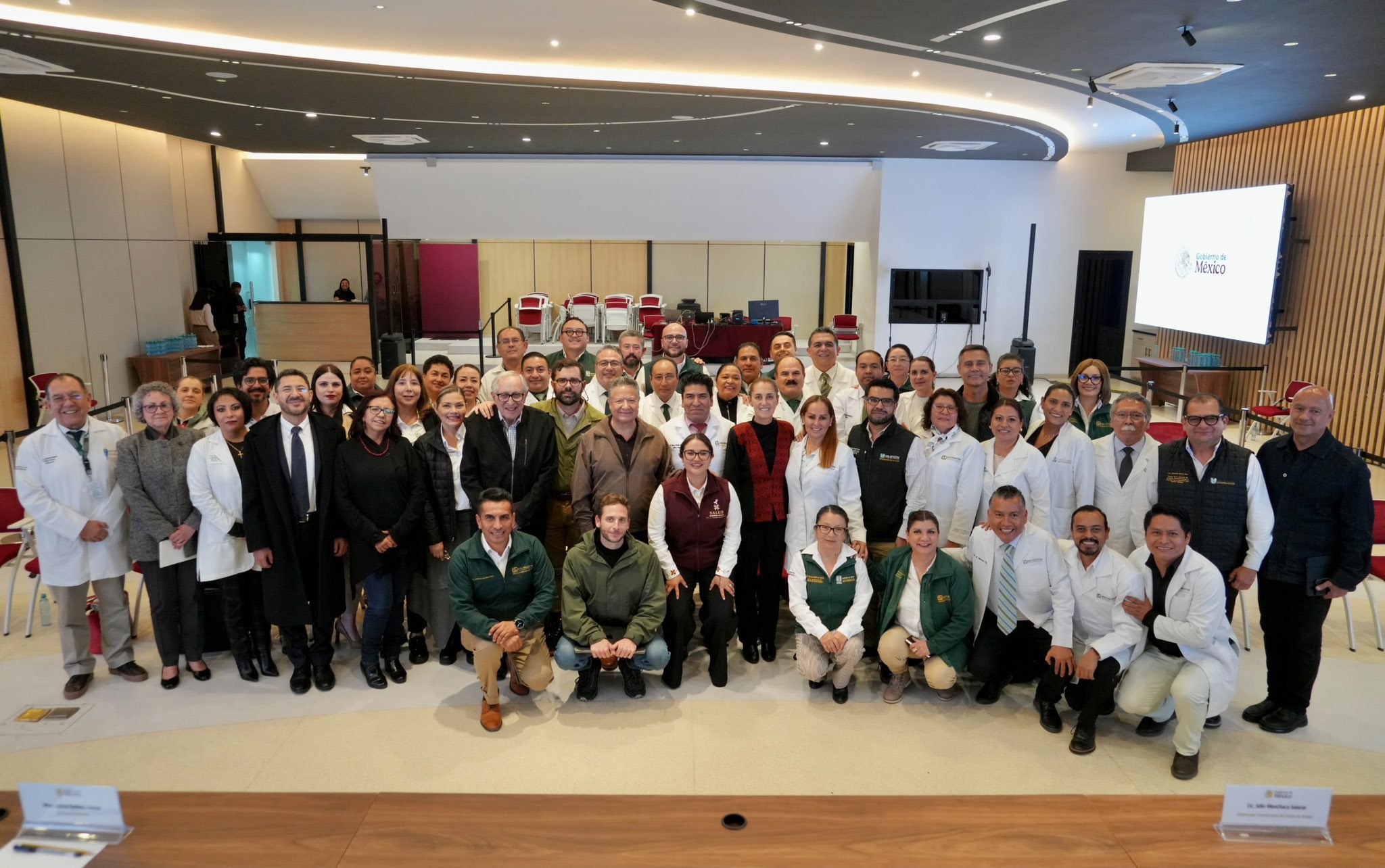 Vista amplia de una reunión de personal médico y directivos hospitalarios en un auditorio, con varias personas levantando las manos