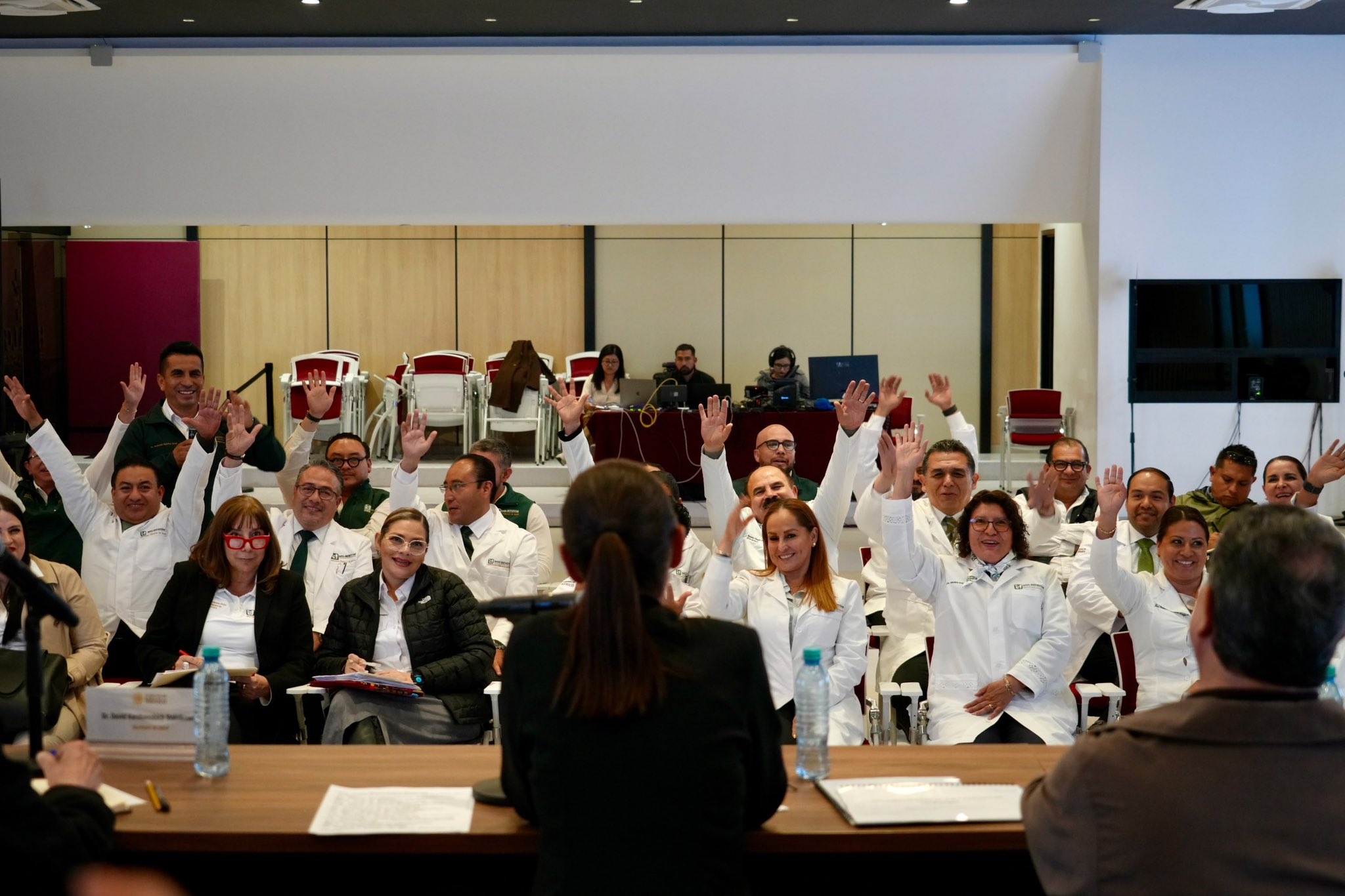 Personal médico y directivos de hospitales con batas blancas levantan las manos durante una reunión en un auditorio