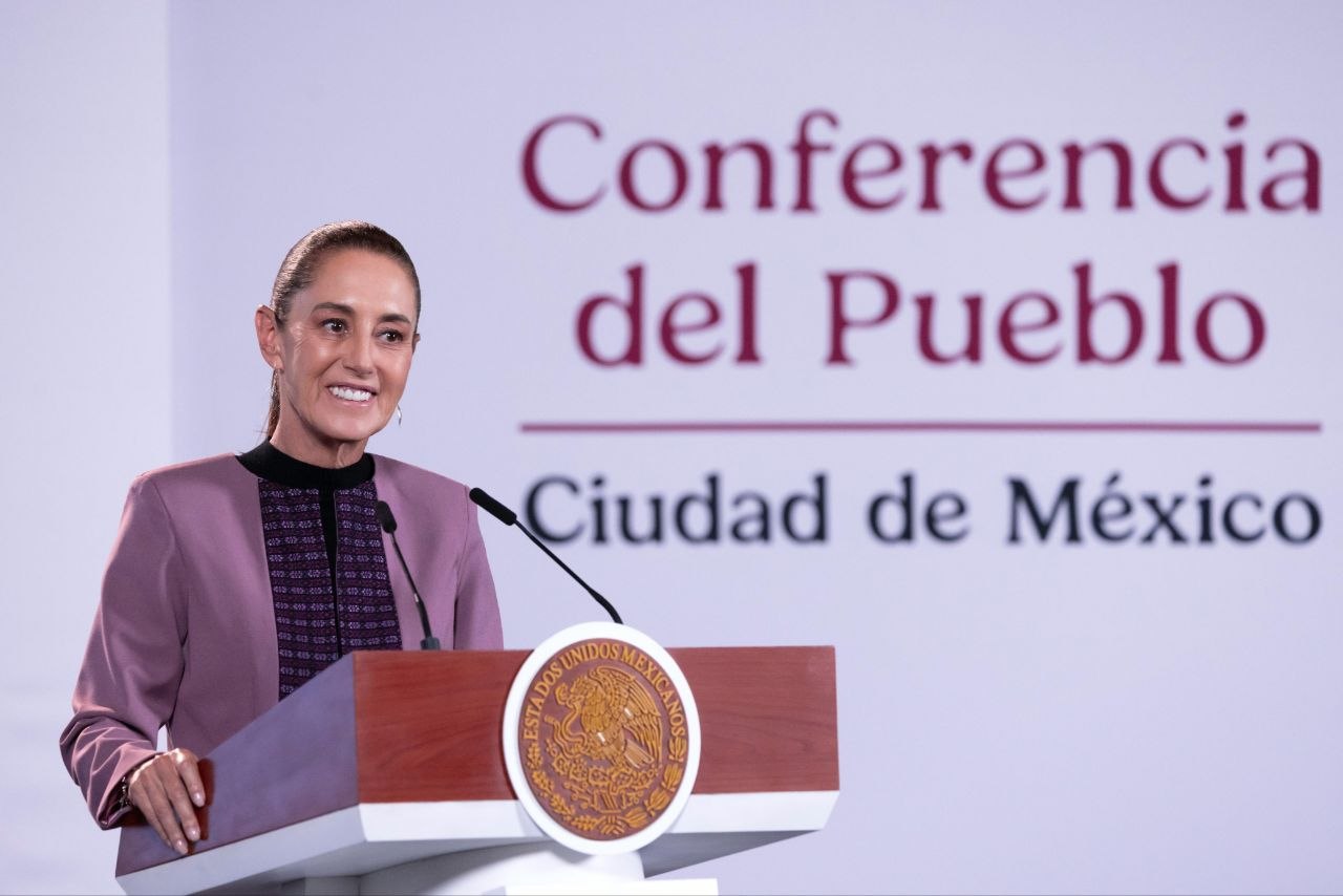 Mujer sonriente habla desde un podio durante la Conferencia del Pueblo en Ciudad de México