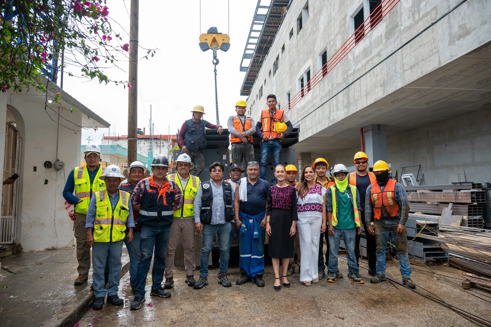 Trabajadores de la construcción con chalecos y cascos posan junto a autoridades frente a un edificio hospitalario en obra