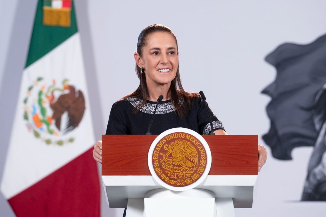 Claudia Sheinbaum durante un mensaje desde un podio con el Escudo Nacional y la bandera de México al fondo