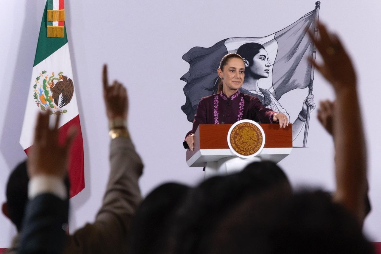 Una mujer habla desde el podio presidencial durante una conferencia de prensa, con una bandera de México a un costado y asistentes en primer plano