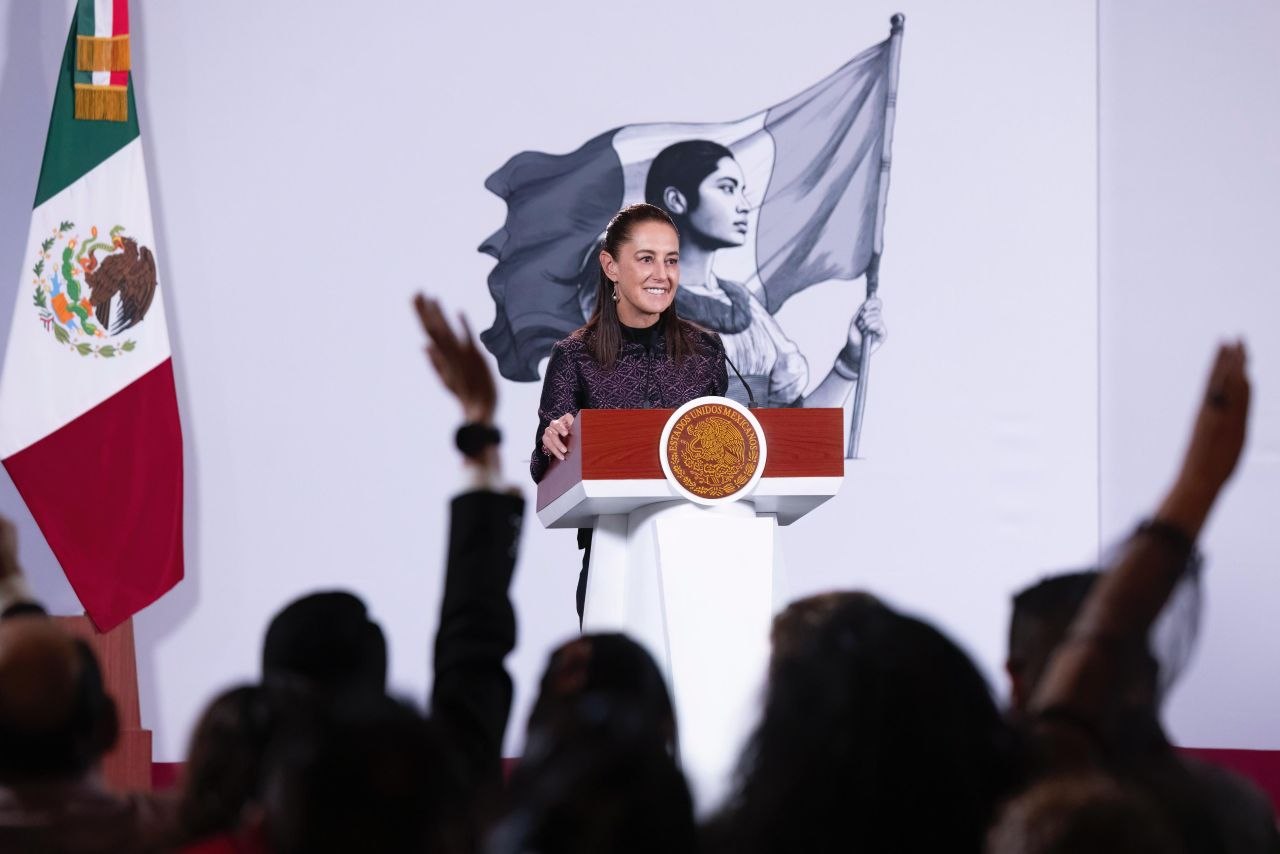 Mujer sonríe desde un podio con el Escudo Nacional mientras varias personas levantan la mano frente a ella
