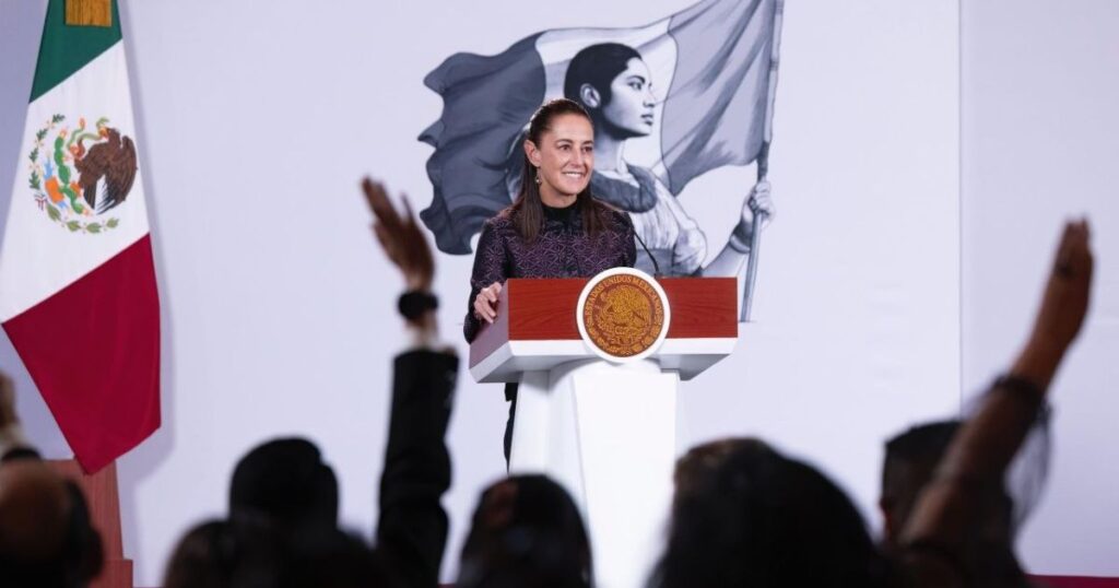 Mujer sonríe desde un podio con el Escudo Nacional mientras varias personas levantan la mano frente a ella