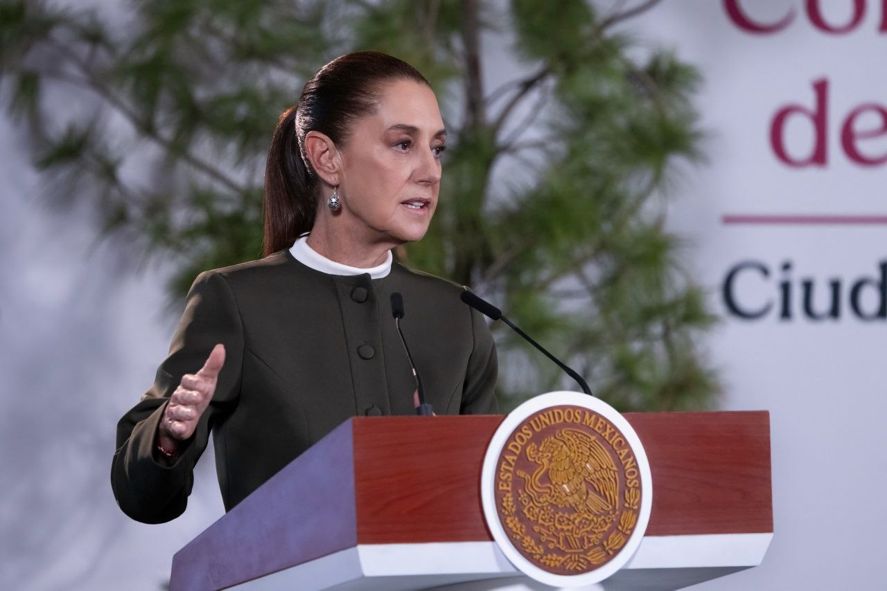 Claudia Sheinbaum habla ante micrófonos desde un podio con el escudo nacional.