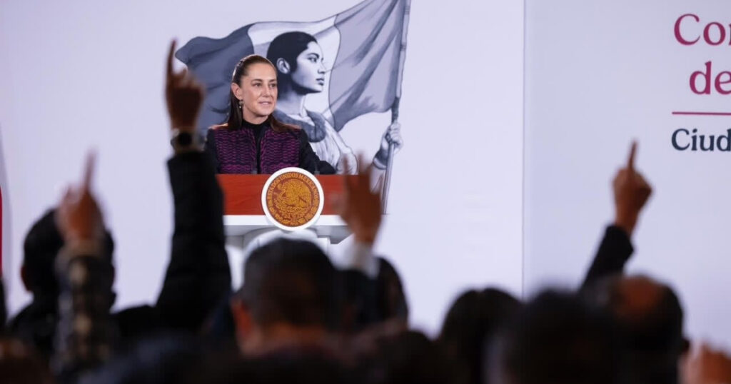 Claudia Sheinbaum habla desde un podio durante una conferencia, con asistentes al frente.